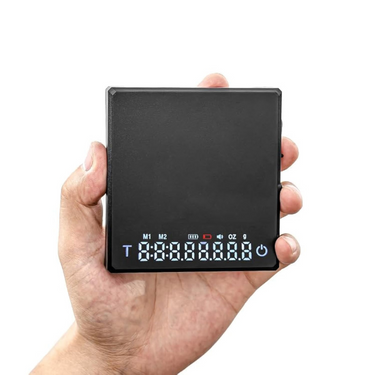 Hand holding the 0.1g High Precision Drip Espresso Scale showing the digital display and stainless steel platform for precise coffee brewing.
